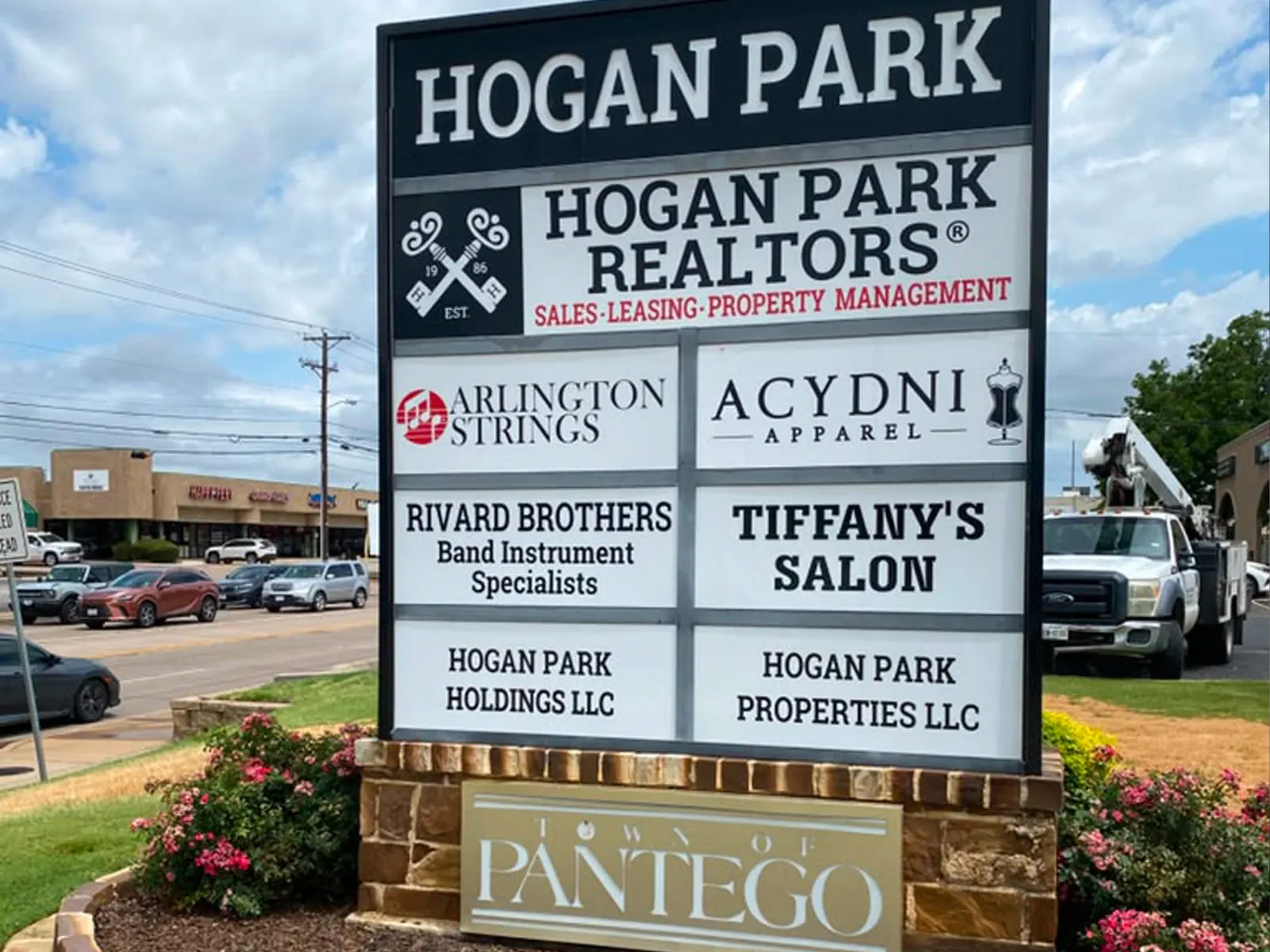 Hogan Park multi-tenant monument sign with tenant panels on a stone base, a bucket truck behind it