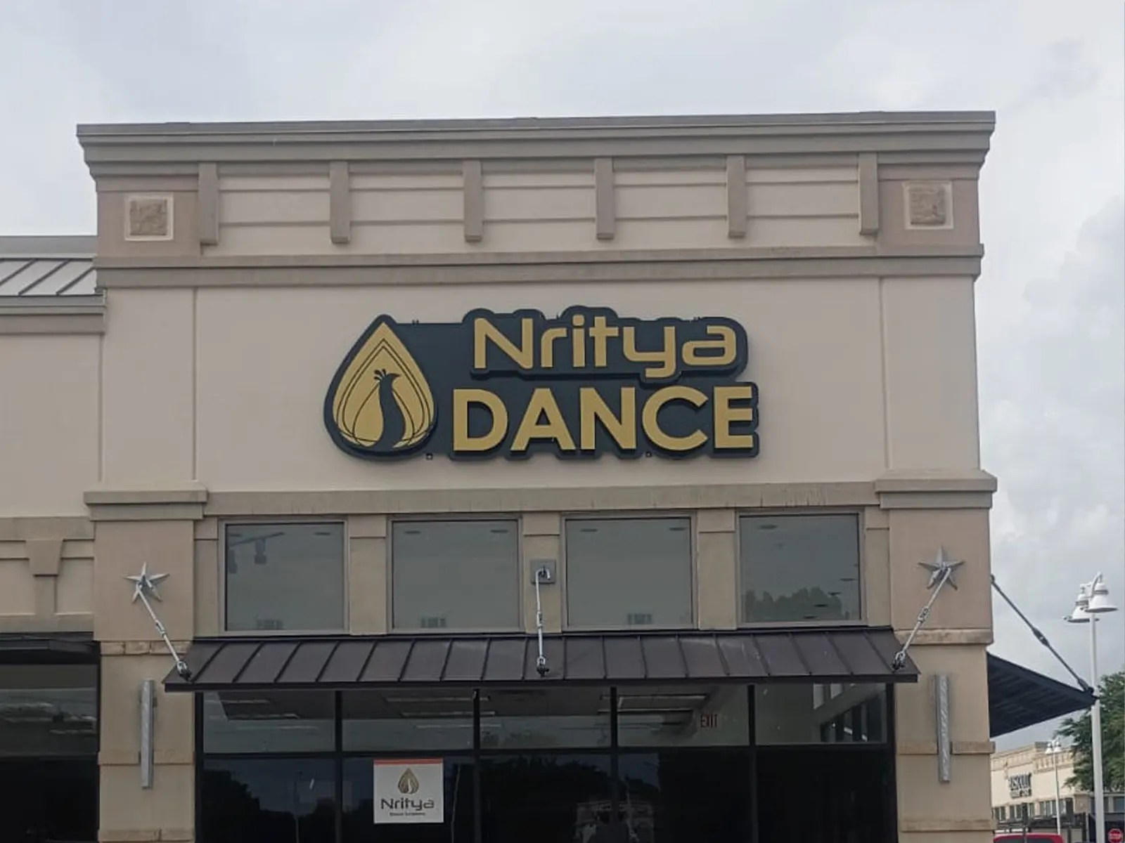Nritya Dance gold letters and peacock logo on a retail facade above a metal awning